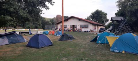 Aufgebaute Zelte; Im Hintergrund grillen Eltern und Kinder